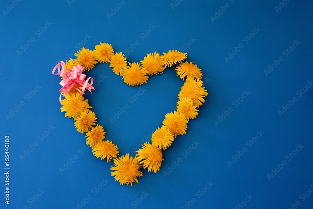 Beautiful bouquet of yellow dandelions with pink hearts and bow on the blue table Beautiful bouquet of yellow dandelions with pink hearts and bow on the blue table