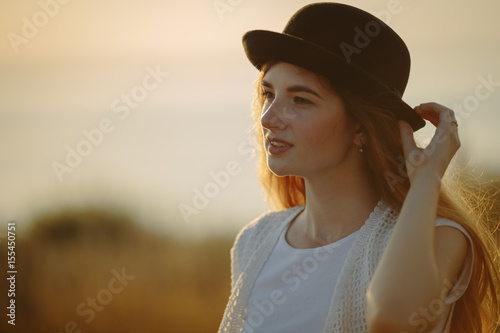 Close up portrait of young pretty woman wearing black hat outdoor on sunset