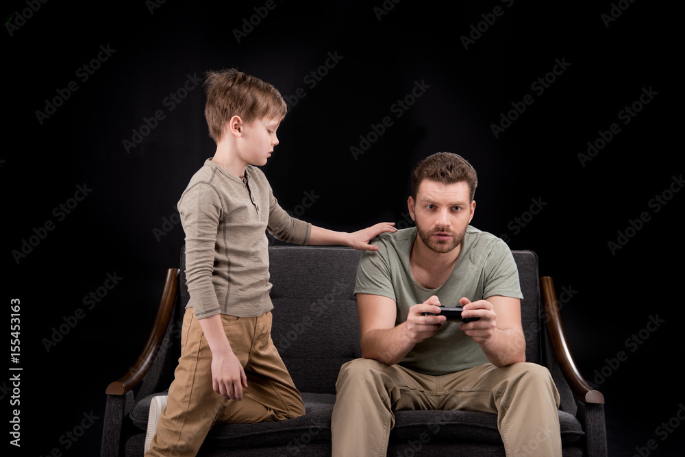 Boy trying to talk with father playing with joystick, family problems concept Boy trying to talk with father playing with joystick, family problems concept