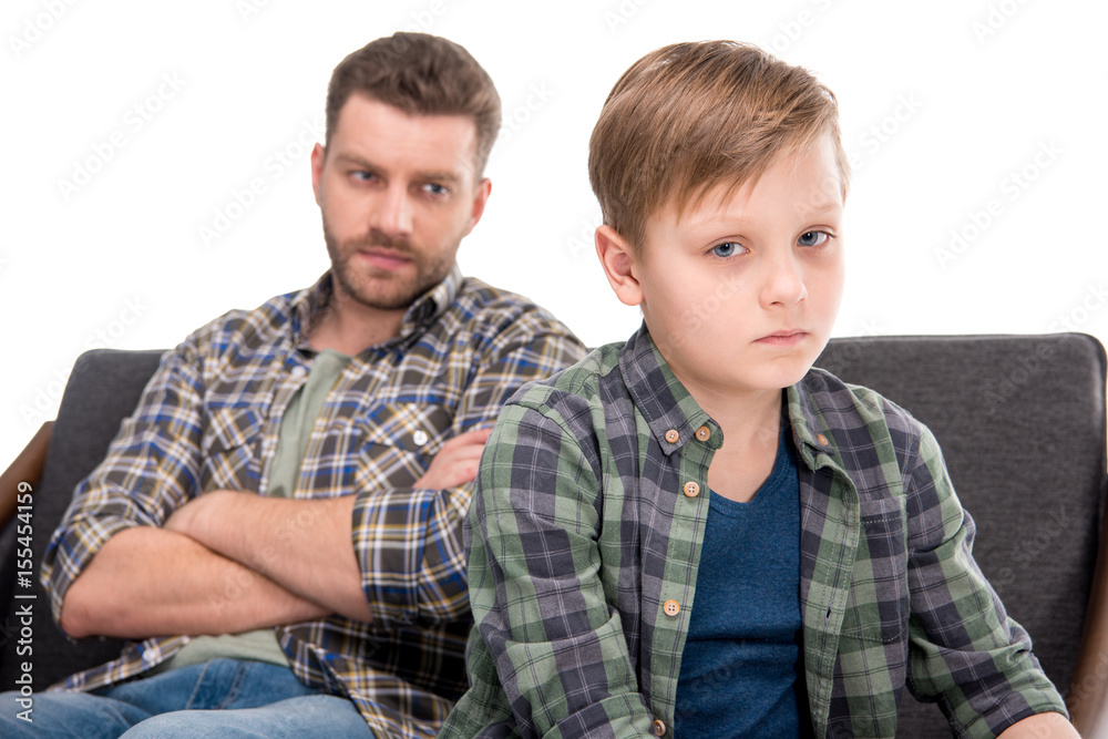 Serious father with crossed arms looking at upset little boy, family problems concept Serious father with crossed arms looking at upset little boy, family problems concept