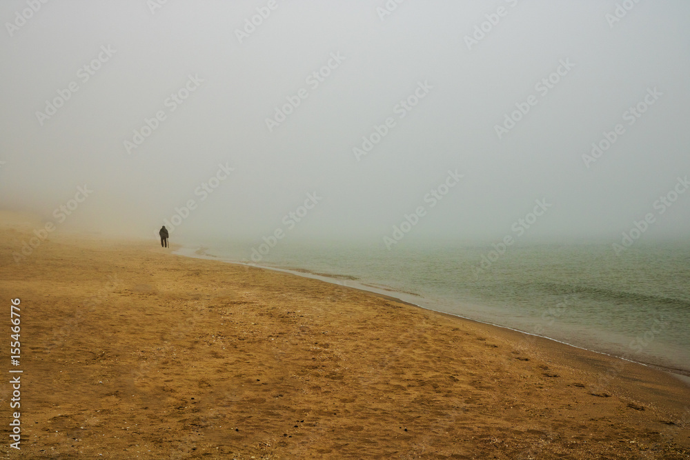 The old man and the sea. Silhouette of an old man with a cane walking on a foggy beach. Minimalist concept.