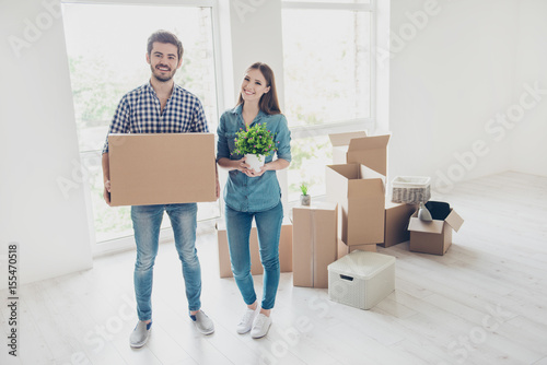 New life, new start, new home for a young family. What a joy! Happy cheerful lovers are unpacking in a new apartment, standing in a casual wear