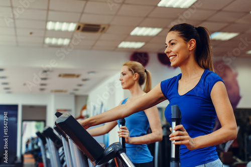 Two young woman exercising on stepper machine at gym