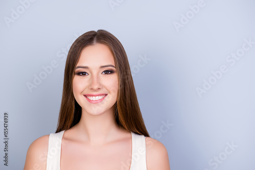 Close up of young gorgeous girl standing on the pure light blue background and smiling, wearing a white casual singlet