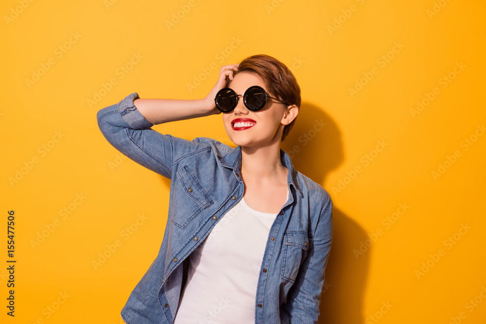 Young cute lady with beaming smile in stylish spectacles is fixing her hair on the bright yellow background. She is full of dreams and fantasies Young cute lady with beaming smile in stylish spectacles is fixing her hair on the bright yellow background. She is full of dreams and fantasies