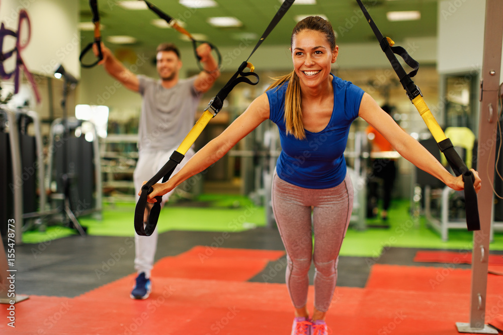 Woman and man exercising with trx in the gym