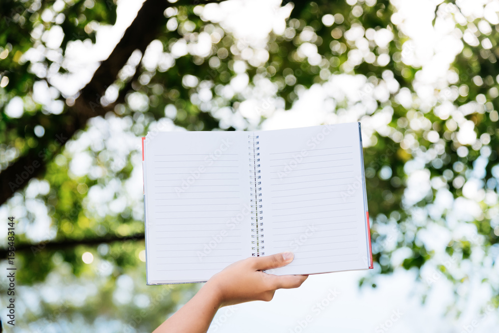 Hand holding a note with a tree in the background in selective focus. Hand holding a note with a tree in the background in selective focus.