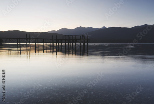 An old wooden pier captured during sunset, the wooden pier was reflected on calm water. © nazmanm