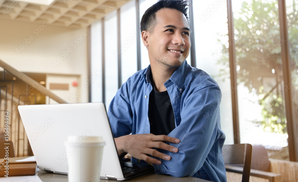 Fototapeta premium Happy young businessman working on laptop while sitting at his working place in office