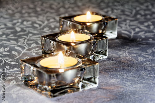 Three lit candles in glass on a white tablecloth