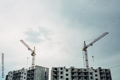 The process of building a multi-storey building. Lifting cranes against the sky.