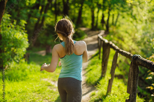 Young woman in mentol shirt workout after jogging. She using her smart phone and listening to music outdoor in summer time.