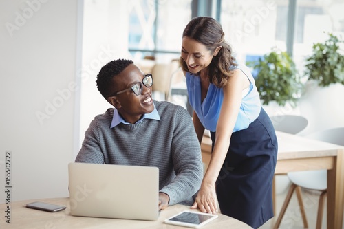 Smiling executives interacting while using laptop