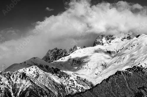Black and white view on snow mountains in clouds in winter sun day