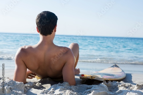 Photography Rear view of shirtless man reclining by surfboard at beach