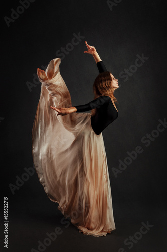 Gymnast in a beige long skirt against a dark background