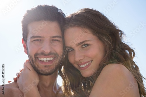 Portrait of smiling young couple embracing against clear sky