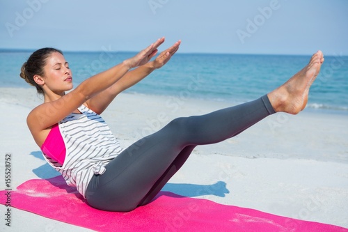 Young woman with eyes closed exercising on mat at beach