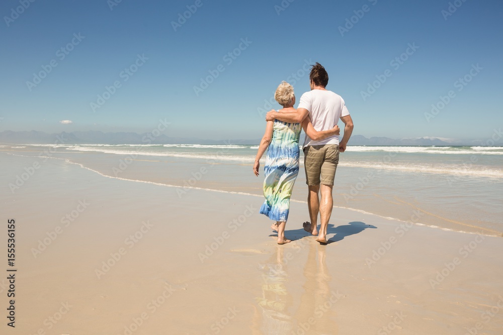 Rear view of woman with son walking on shore against clear sky