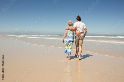 Rear view of woman with son walking on shore against clear sky