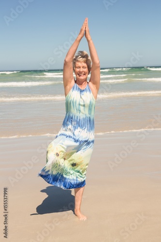 Senior woman exercising while standing at beach photo