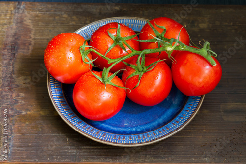 Tomatoes on the twig, dark blue plate. Isolated. Wooden background background.