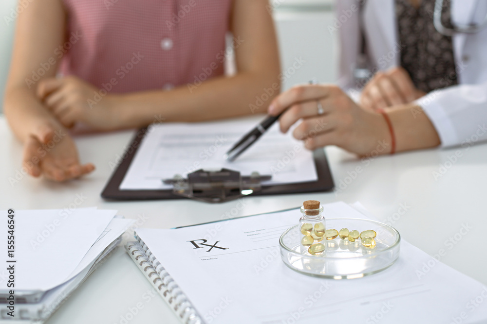 Medical prescription form, capsules and pills are lying against the background of a doctor and patient discussing health exam results Medical prescription form, capsules and pills are lying against the background of a doctor and patient discussing health exam results