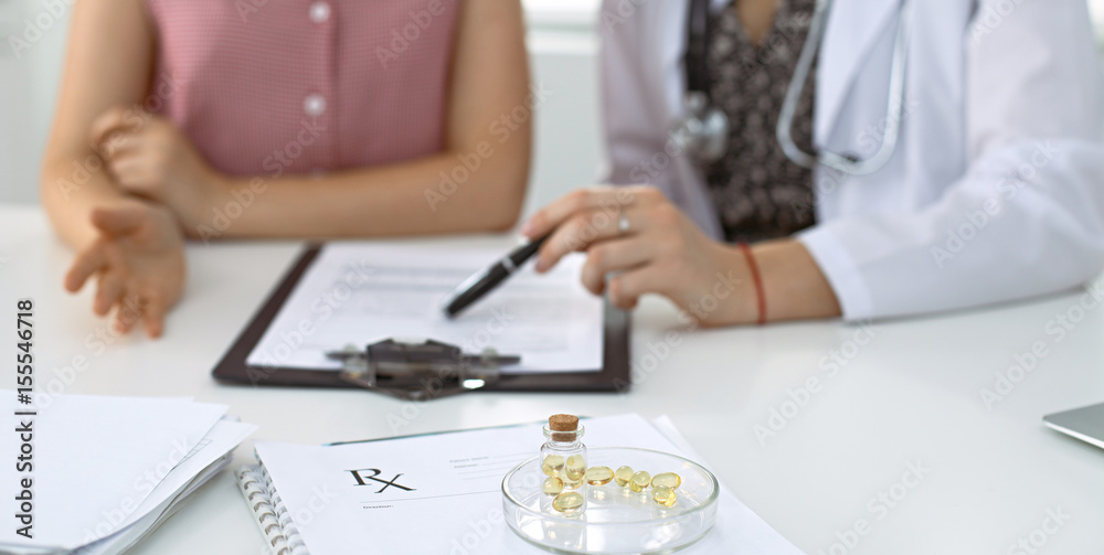 Medical prescription form, capsules and pills are lying against the background of a doctor and patient discussing health exam results Medical prescription form, capsules and pills are lying against the background of a doctor and patient discussing health exam results