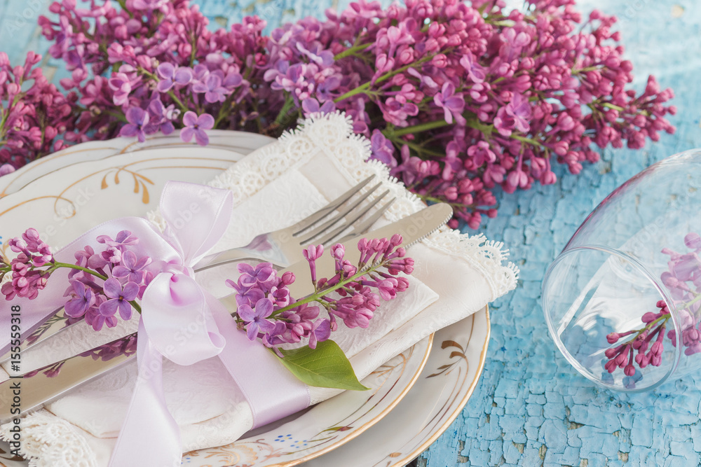 Tableware and silverware with violet lilac on the wooden background Tableware and silverware with violet lilac on the wooden background