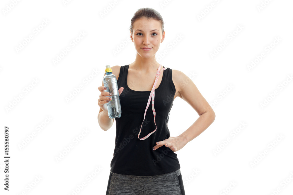 cute young fitness girl in black shirt looks into the camera and keep the measuring tape and water at hand cute young fitness girl in black shirt looks into the camera and keep the measuring tape and water at hand