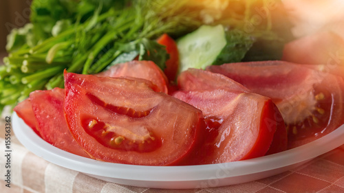 Tomatoes cut into chunks for salad on the background of the cucumbers and greens on a Sunny day.