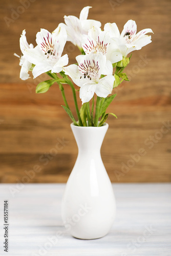 Flowers in a ceramic vase. Daisies and lilies. Vertical shoot.