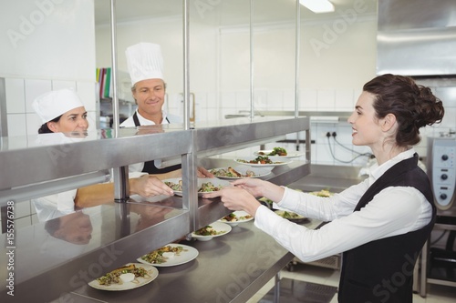 Chef handing food dish to waitress at order station photo