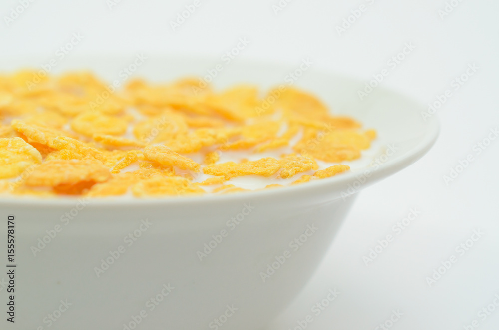 Cornflakes with milk on a spoon in a bowl on a light background.