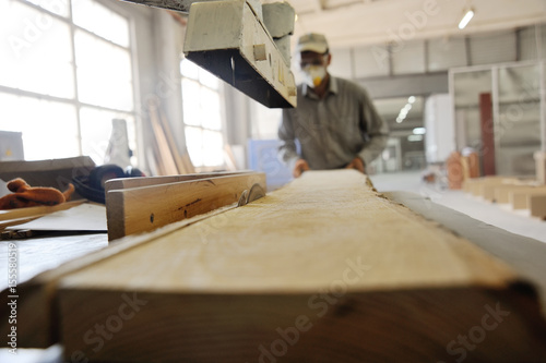 Carpenter in overalls works in a workshop with a wooden beam