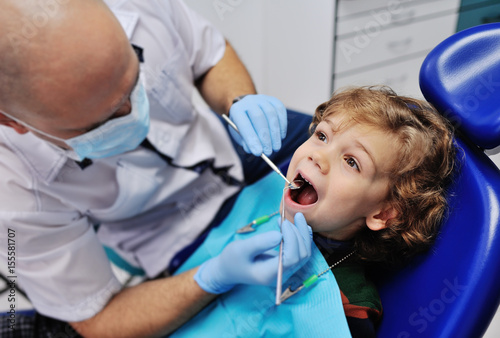 Male dentist examines the teeth of the patient cheerful child with curly red hair. Moloi boy smiling in dentist s chair. child mouth wide open in the dentist s chair