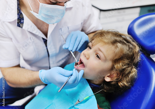 Male dentist examines the teeth of the patient cheerful child with curly red hair. Moloi boy smiling in dentist s chair. child mouth wide open in the dentist s chair