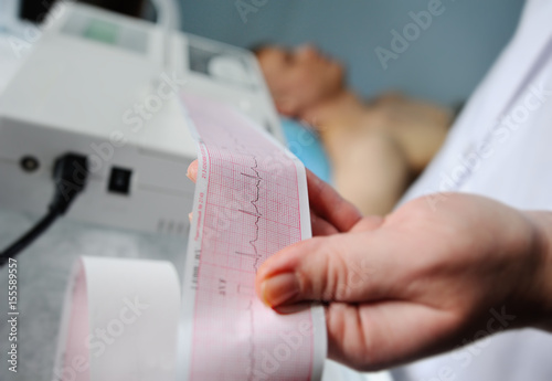 Electrocardiogram, ecg in hand. Clinic cardiology heart rhythm and pulse test closeup. Cardiogram printout. photo