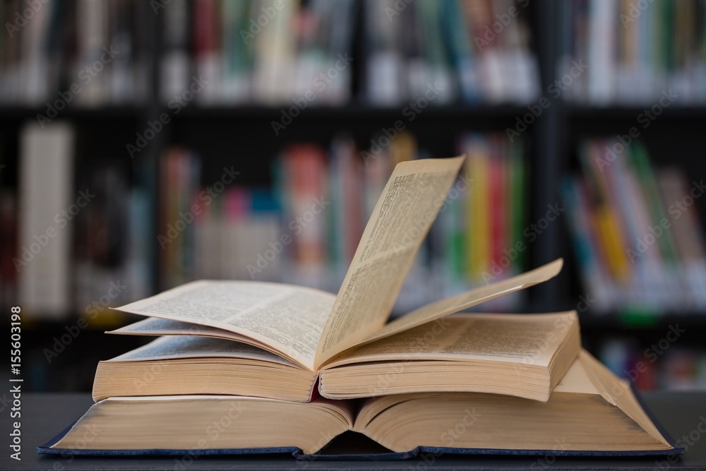 Stack of books on table against shelf Stack of books on table against shelf