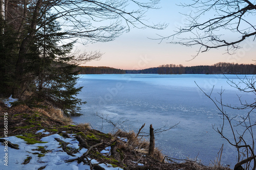 Calm evening on the frozen lake shore. Dawn light in the sky. Early spring nature landscape