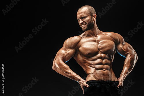 Strong bald bodybuilder with six pack. Strong bodybuilder man with perfect abs, shoulders,biceps, triceps and chest, personal fitness trainer flexing his muscles photo