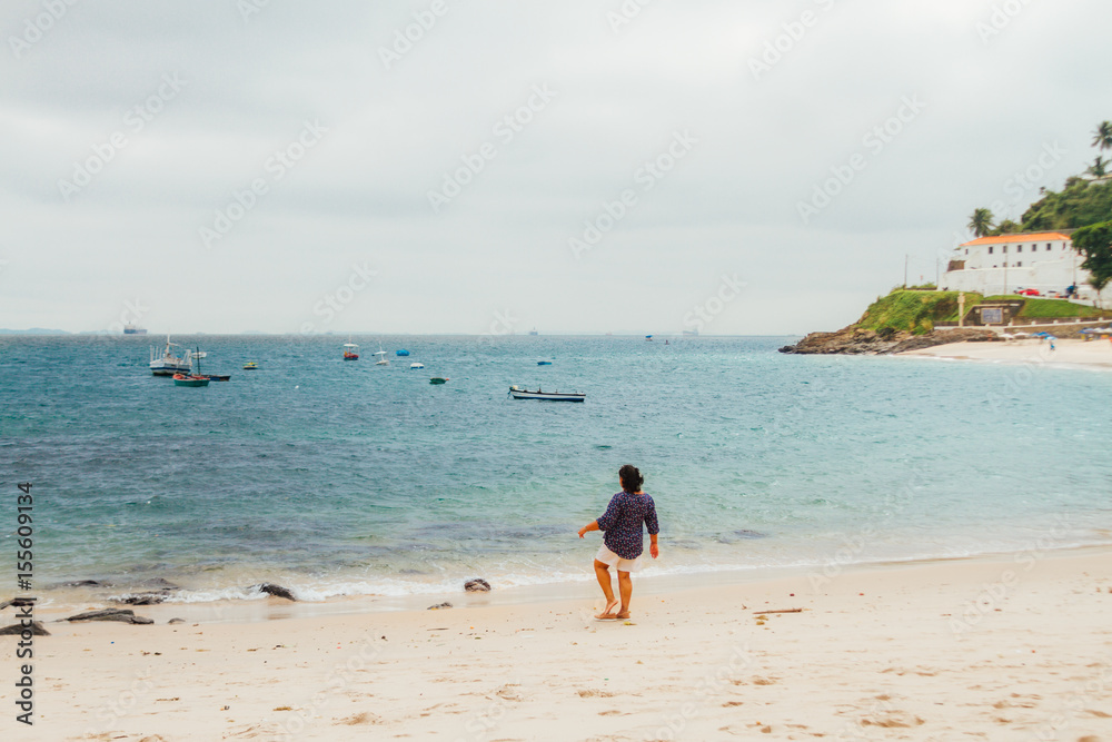 Woman entering the sea with boats in the water on a beach in Salvador de Bahia, Brazil Woman entering the sea with boats in the water on a beach in Salvador de Bahia, Brazil