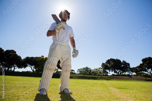 Confident player with cricket bat standing against sky