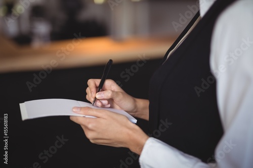 Mid-section of waitress writing order on notepad
