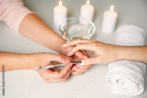 Nail care. Closeup of beautiful woman hands getting manicure in spa salon. Female manicurist cleaning cuticle with professional manicure pusher tool. Cosmetic procedure.