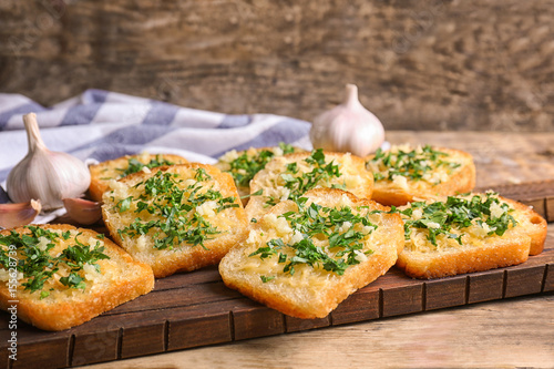 Tasty bread slices with garlic, cheese and herbs on wooden cutting board