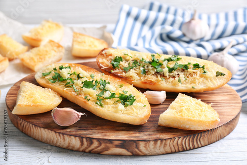 Tasty bread slices with garlic, cheese and herbs on wooden cutting board