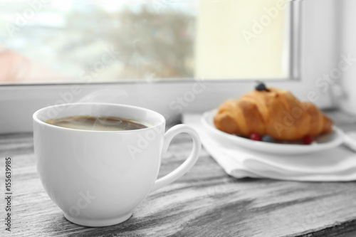 Cup of coffee and croissant on windowsill