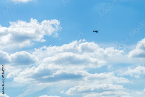 Blue sky with sculpted clouds on the background with real tinny helicopter flying on the left side
