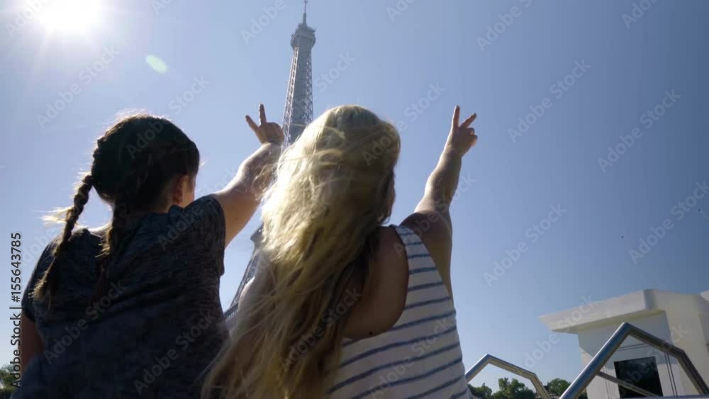 Adventurous Young Women Hold Up Peace Signs As Their Tour Boat Floats Past The Eiffel Tower In Paris, France